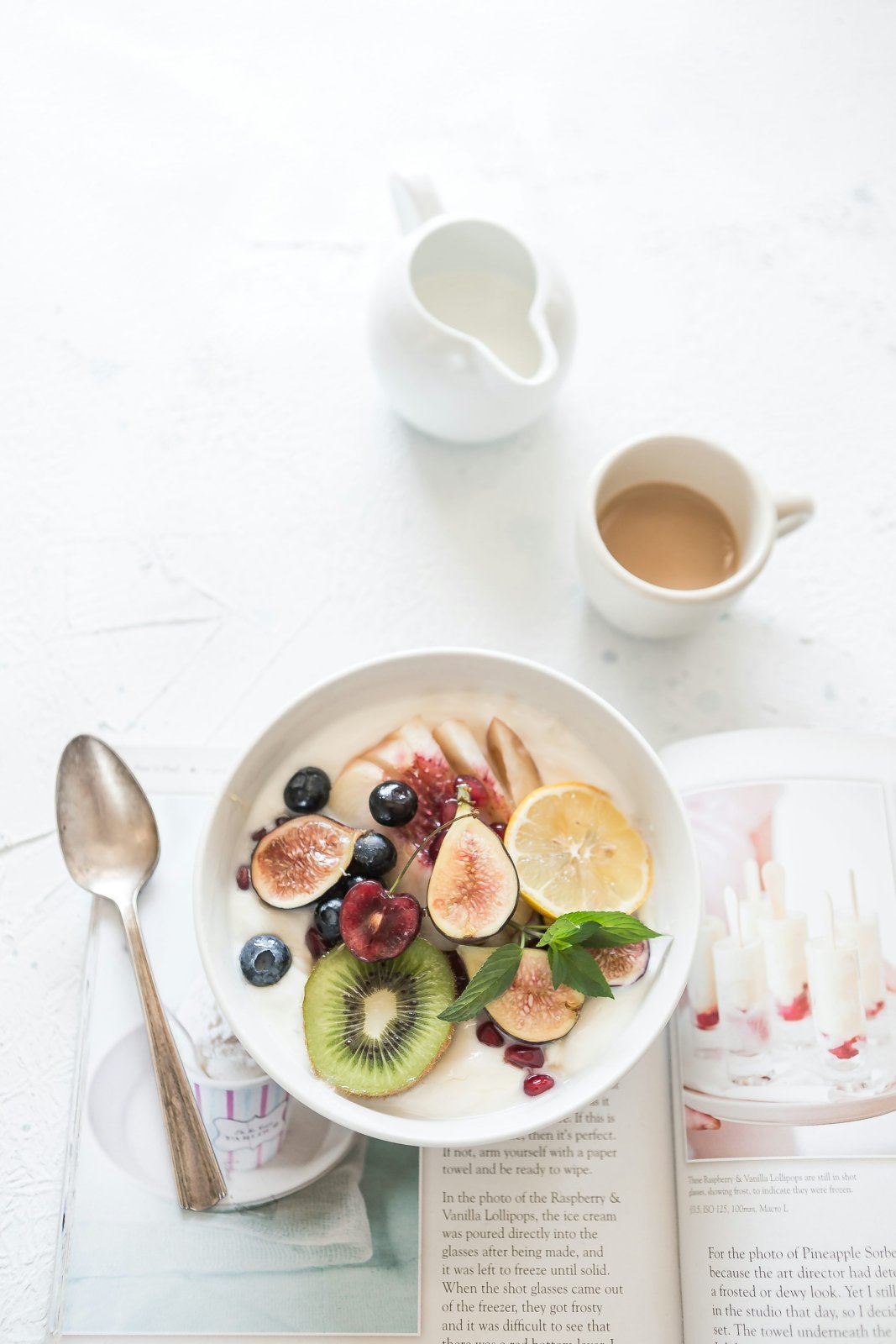 A bowl of yogurt topped with sliced fruit beside a coffee cup.