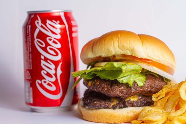 A can of Coca-Cola next to a fast food burger.