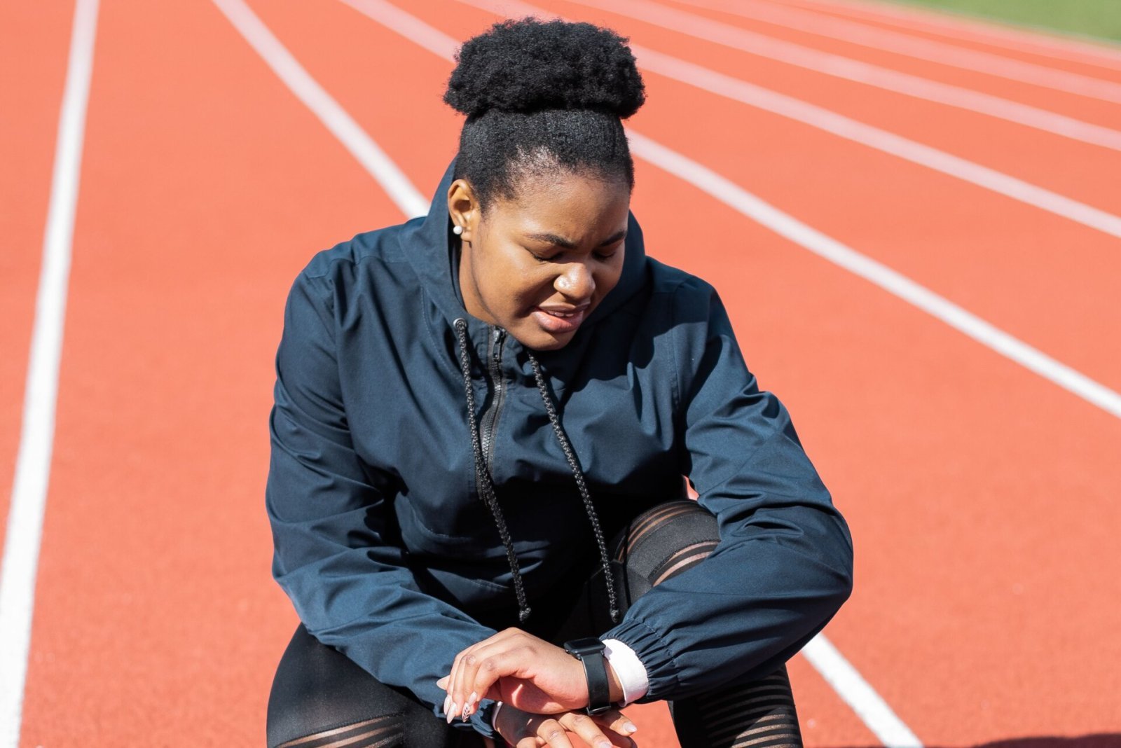 A woman in sportswear checks her smartwatch while resting on an outdoor running track.