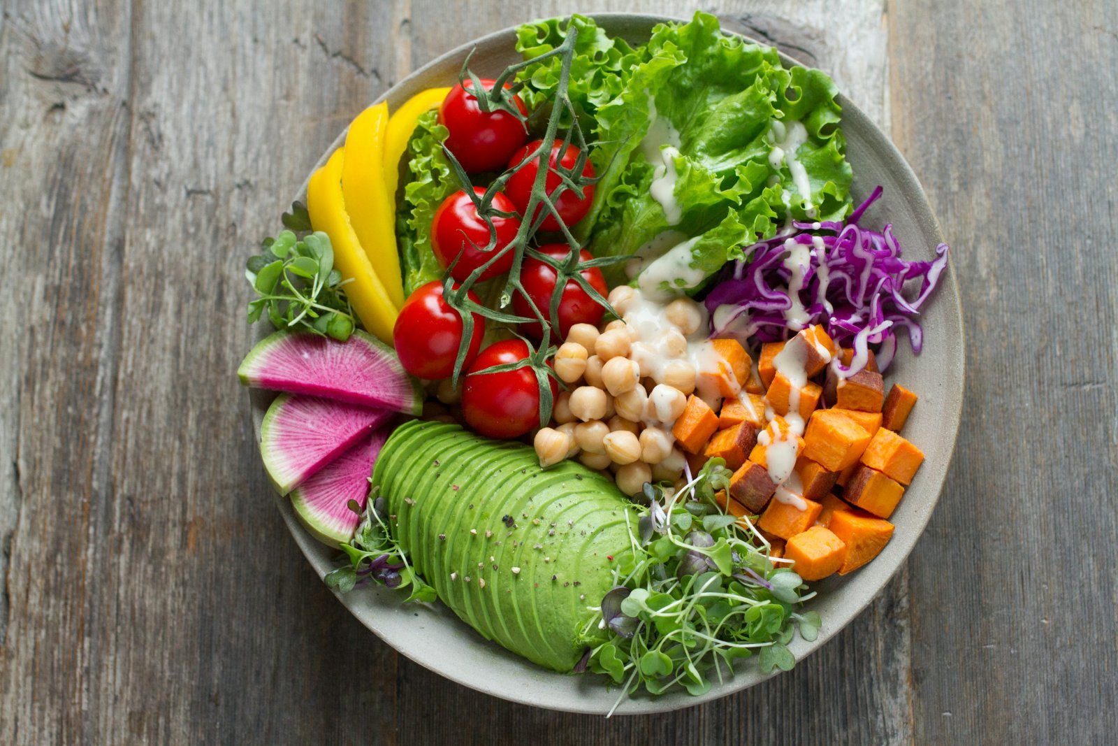 A colorful bowl of salad with leafy greens, chickpeas, tomatoes and avocado.
